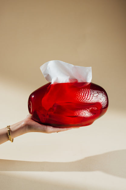 Red glass tissue holder with a white tissue on a beige background