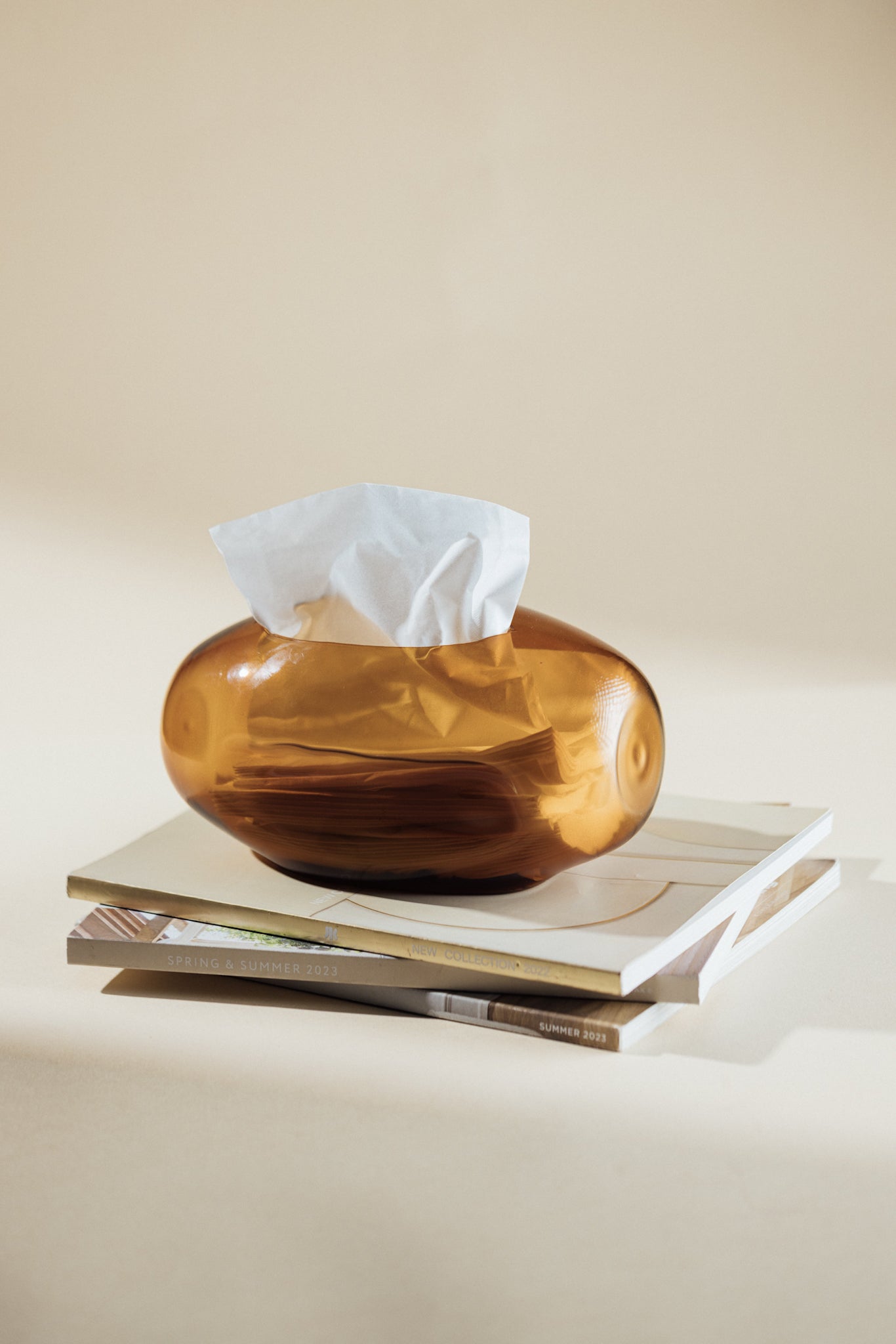 Brown glass tissue box with white tissues on a beige surface