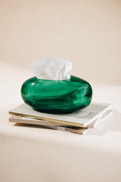 Green glass tissue holder with tissues on a stack of books against a beige background